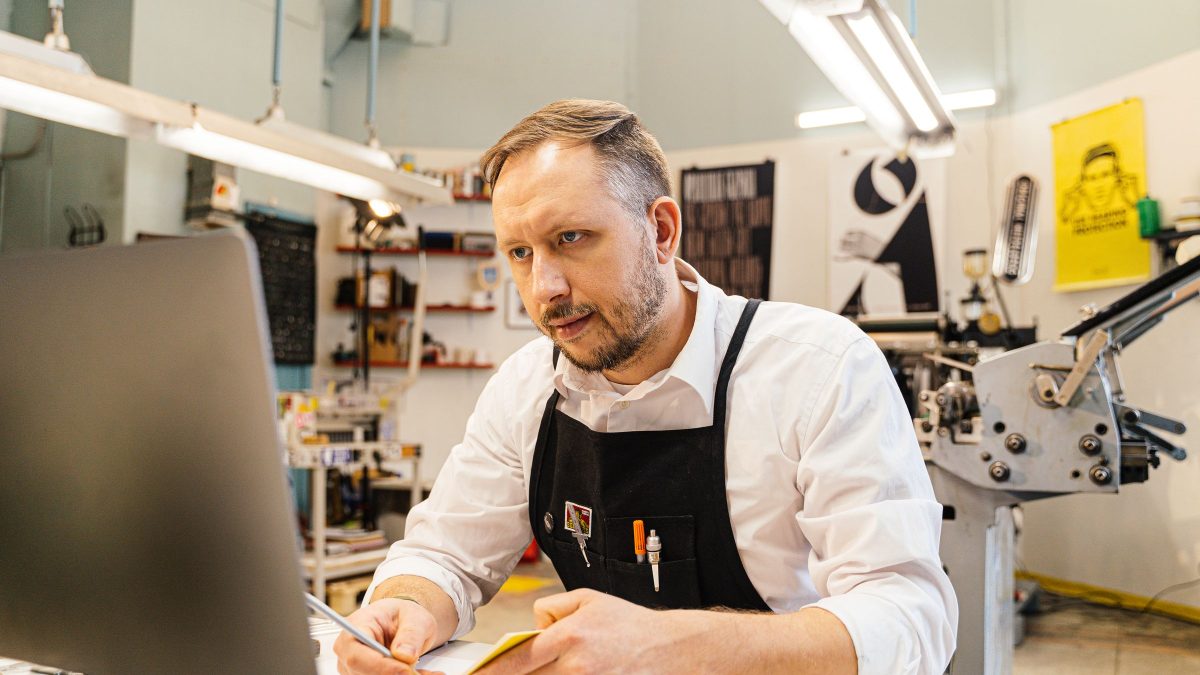 A shop owner using a tablet at the counter of a small store.