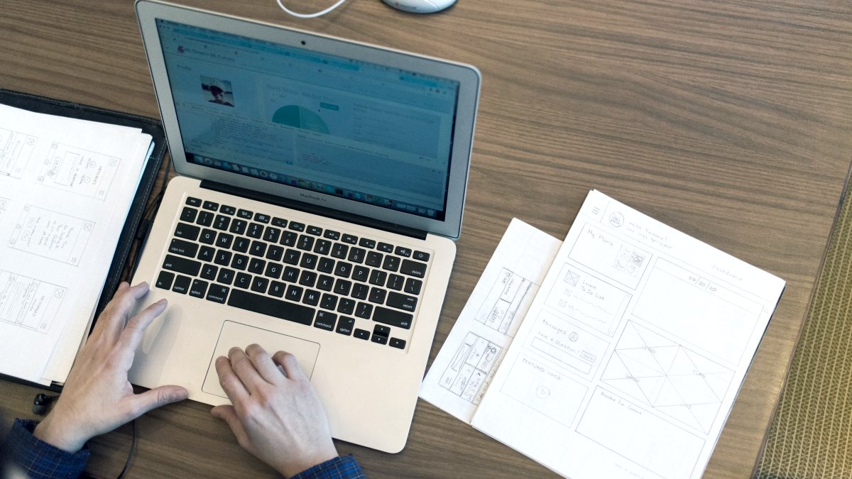 An overhead view of someone working at a laptop with documents beside it.